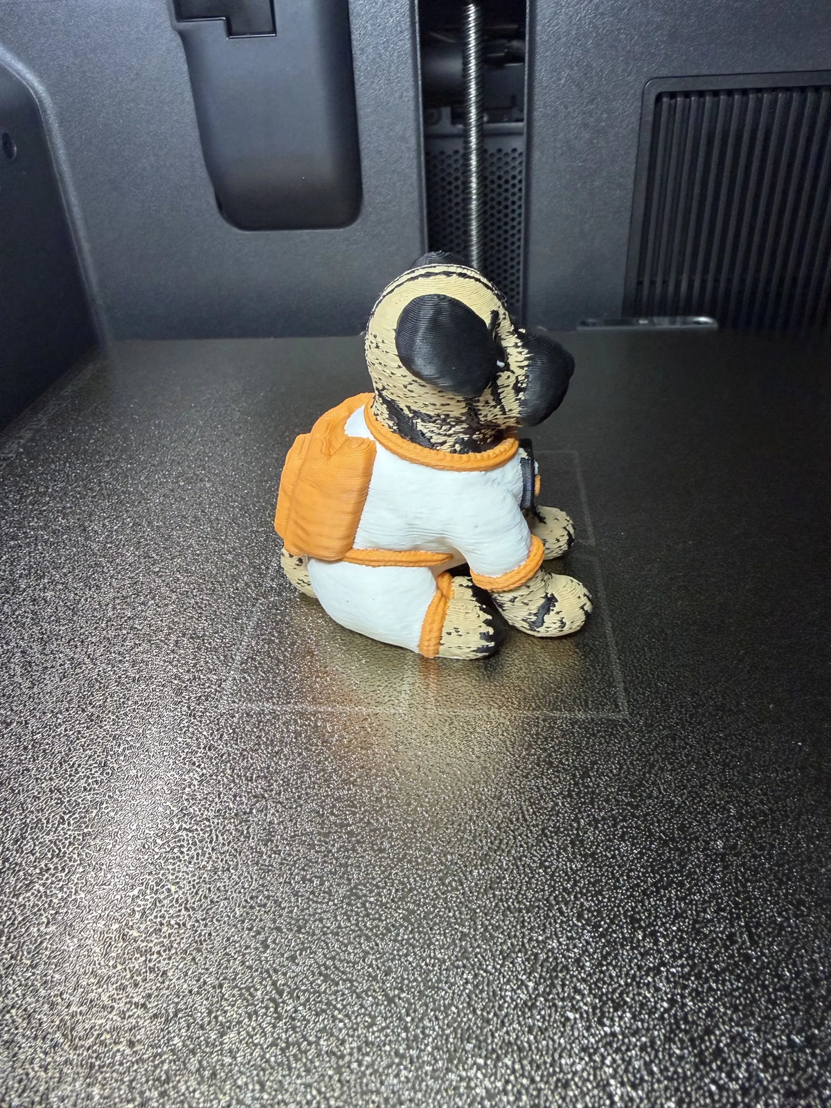 Angled rear view of Astro Dog in an astronaut-style suit beside a 3D printer