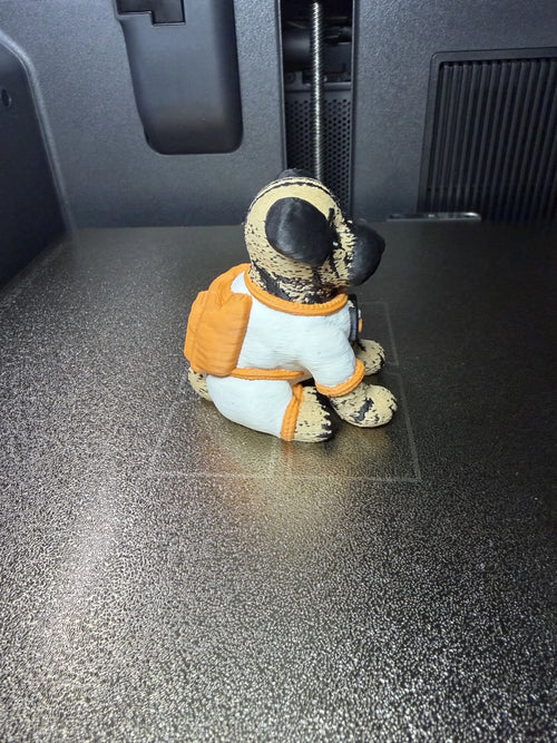 Angled rear view of Astro Dog in an astronaut-style suit beside a 3D printer